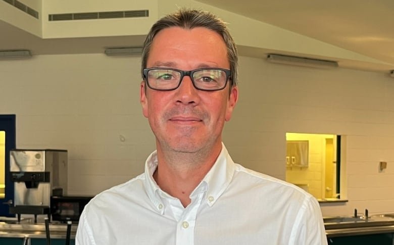 A man smiles. He stands in front of a cafeteria food counter.