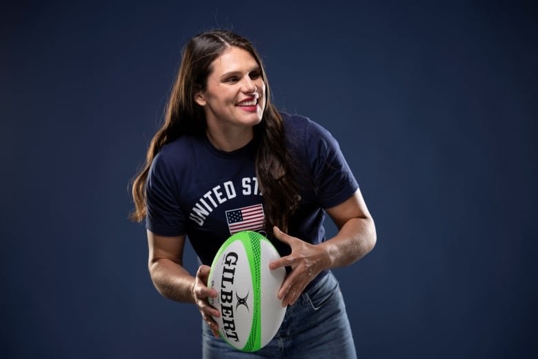 A woman smiles with a rugby ball.