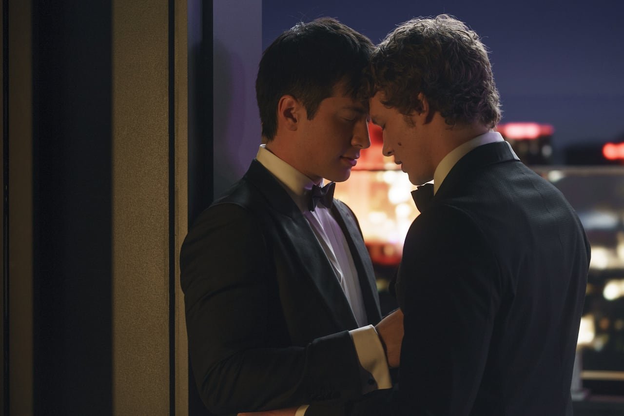Two men in tuxedos leaning heads together on a rooftop.